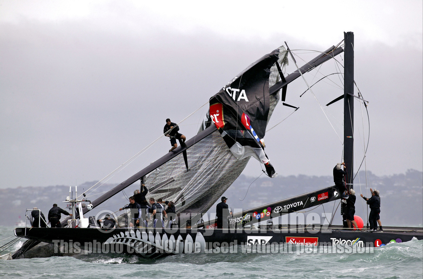 03_0256D ©Th.Martinez - Auckland (NZ) . America's Cup 2003. 28th February 2003. Day 4 .Alinghi (SUI 64) vs Team NZ (NZL 82) .Team NZ's boat dismast 57 minutes after the start in only 18 knots of windwith a swell of 1.5 m. Team NZ crew trying to take off the main sail from the broken mast. Alinghi is leading Team NZ  4-0 after 4 races..
