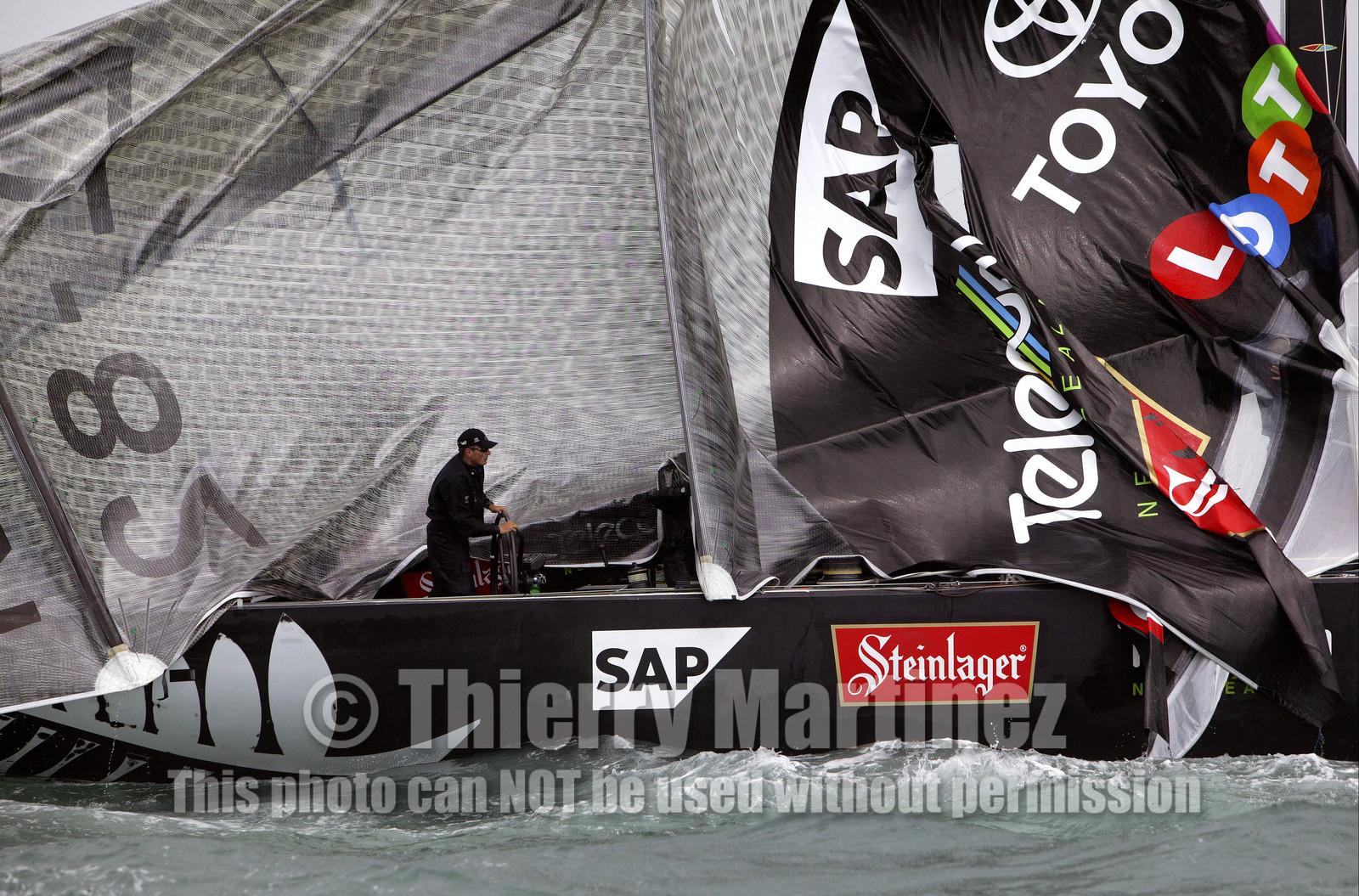 03_0254D ©Th.Martinez - Auckland (NZ) . America's Cup 2003. 28th February 2003. Day 4 .Alinghi (SUI 64) vs Team NZ (NZL 82) .Team NZ's boat dismast 57 minutes after the start in only 18 knots of windwith a swell of 1.5 m. Dean Barker still at the helm, with main sail and mast on deck. Alinghi is leading Team NZ  4-0 after 4 races.